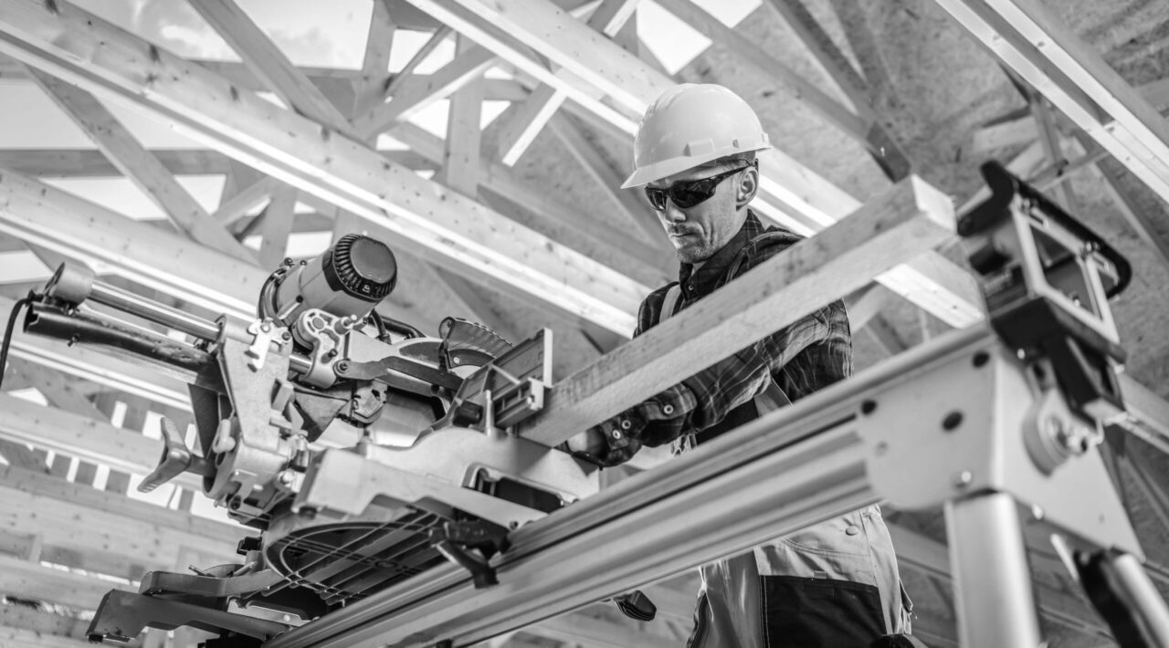Caucasian Construction Contractor Cut to Size Wooden Structure Elements Using Powerful Wood Saw. Construction Industry Theme.